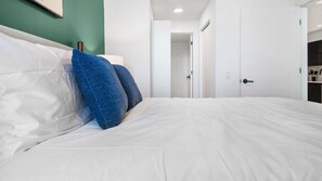 A bedroom with a bed, pillows, a nightstand, a wardrobe, and a bathroom visible in the background. - Landing | Chic 1BD, Rooftop Lounge, Gym (Orlando)