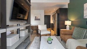 A modern living room with a flat-screen TV, a sofa, a coffee table, and a dining area. - Landing | Stylish Studio, Gym, Courtyard (Orlando)