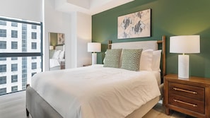 A hotel room with a large bed, two bedside tables with lamps, a green accent wall, and a window with a view of buildings. - Landing | Stylish Studio, Gym, Courtyard (Orlando)