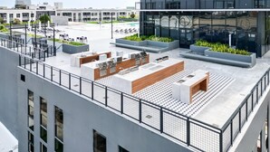 Una terraza en la azotea con mobiliario exterior, piscina y un edificio moderno al fondo.
