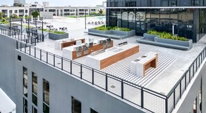 A rooftop terrace with outdoor seating, a pool, and a modern building in the background. - Landing | Stylish Studio, Gym, Courtyard (Orlando)