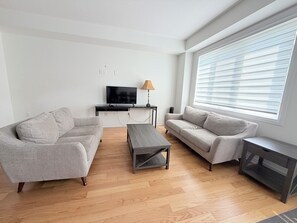 Ein modernes Wohnzimmer mit zwei Sofas, einem Couchtisch, einem Fernseher und einem Fenster mit Jalousien.