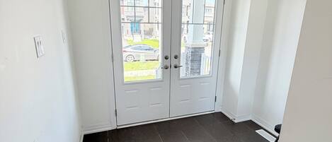 Habitación con puerta doble, suelo de baldosas oscuras y vistas al exterior.