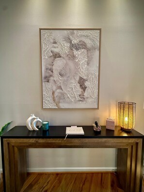 A reception desk with a framed abstract artwork, a candle, a tissue box, and a small figurine. - The Pause, 4-bedroom Modern Timber Retreat in Berkeley Springs (Berkeley Springs)