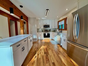 A modern kitchen with white cabinetry, stainless steel appliances, and a wooden floor. - The Pause, 4-bedroom Modern Timber Retreat in Berkeley Springs (Berkeley Springs)