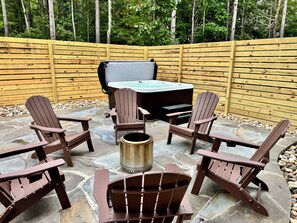 An outdoor patio with Adirondack chairs, a hot tub, and a stone floor. - The Pause, 4-bedroom Modern Timber Retreat in Berkeley Springs (Berkeley Springs)