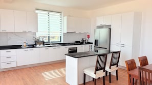 A modern kitchen with white cabinets, a black countertop, and a dining area with wooden chairs. - Joli Penthouse 60m² Rooftop Terrace, 360° View (Sal)