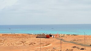 Una zona costera amb un edifici petit, un camí de terra i el mar al fons.
