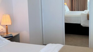 Et hotelværelse med en seng, et natbord med en lampe og et spejl, der viser et andet værelse med seng og gardiner.