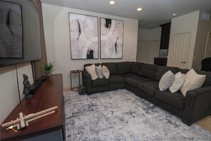 A living room with a sectional sofa, a small side table, a decorative cross, and abstract wall art. - Spacious 3-bedroom condo in gorgeous Tucson with AC and pool (Tucson)