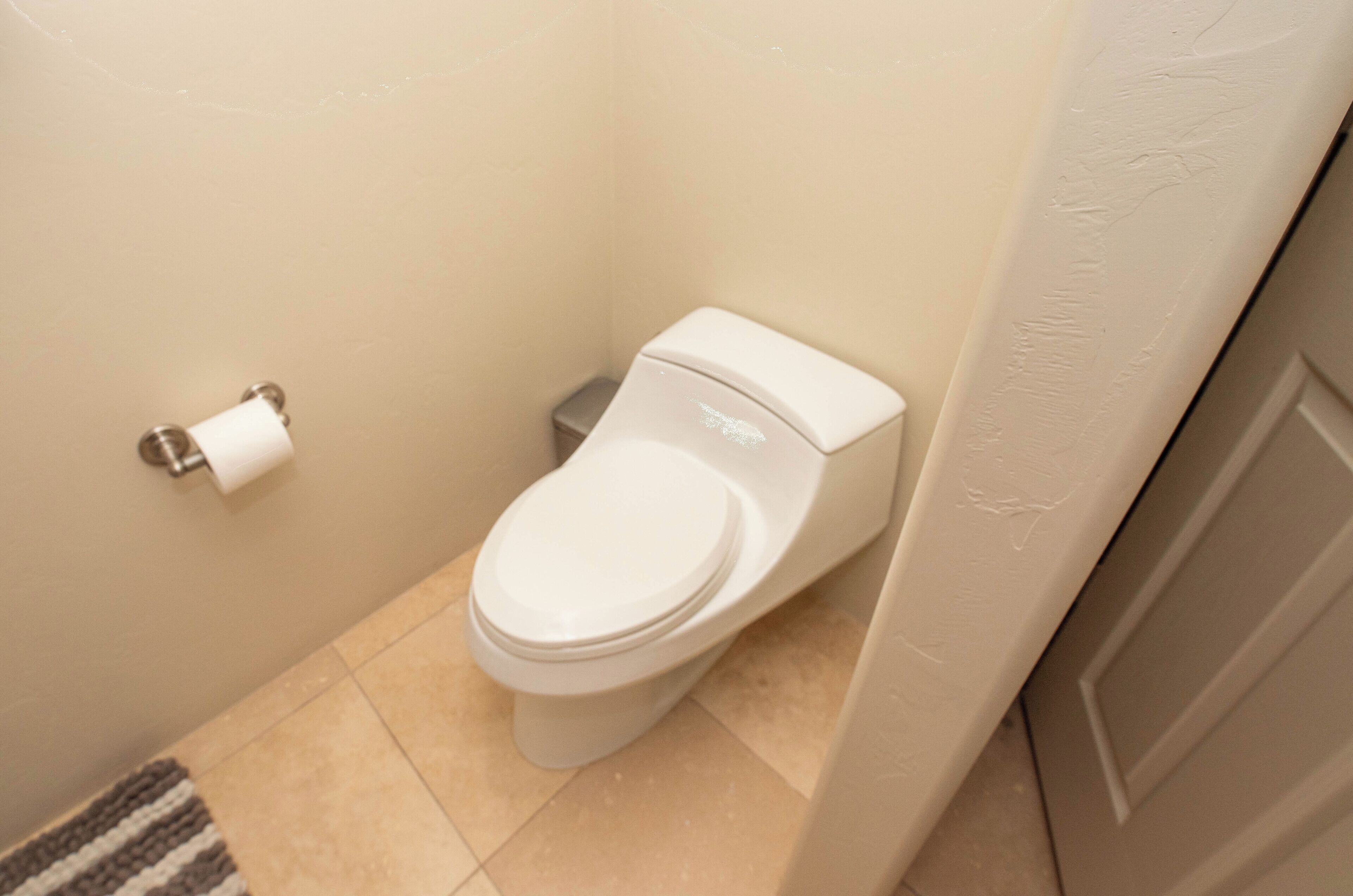 A standard toilet in a bathroom with a plain wall and a small trash bin beside it.
