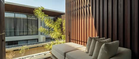 Un espace extérieur moderne aménagé avec un canapé et des coussins, un mur en bois à lattes et une vue sur un bâtiment doté de grandes fenêtres.