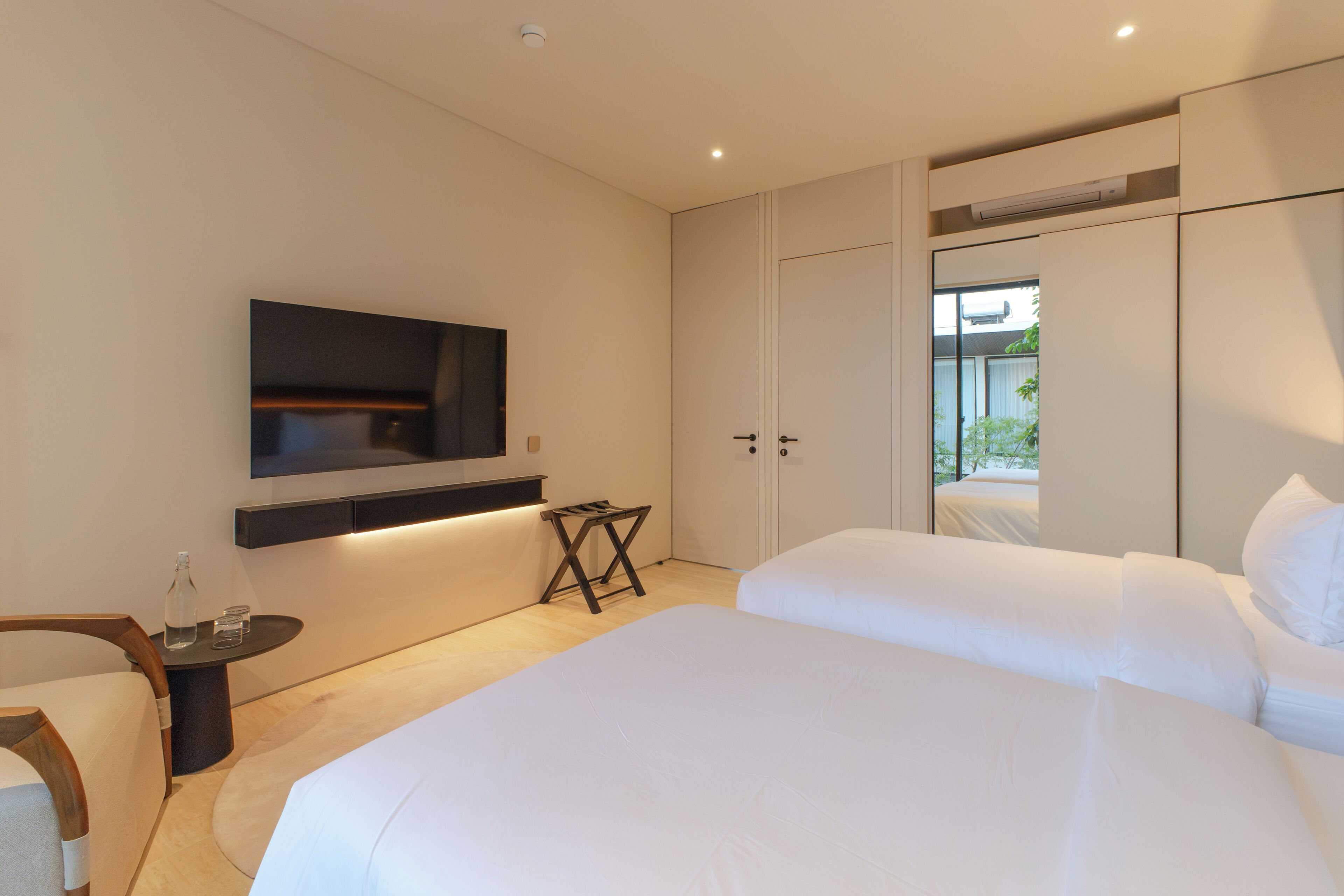 Ein modernes Schlafzimmer mit einem großen Bett, einem an der Wand montierten Fernseher und einem kleinen Tisch mit einer Flasche.