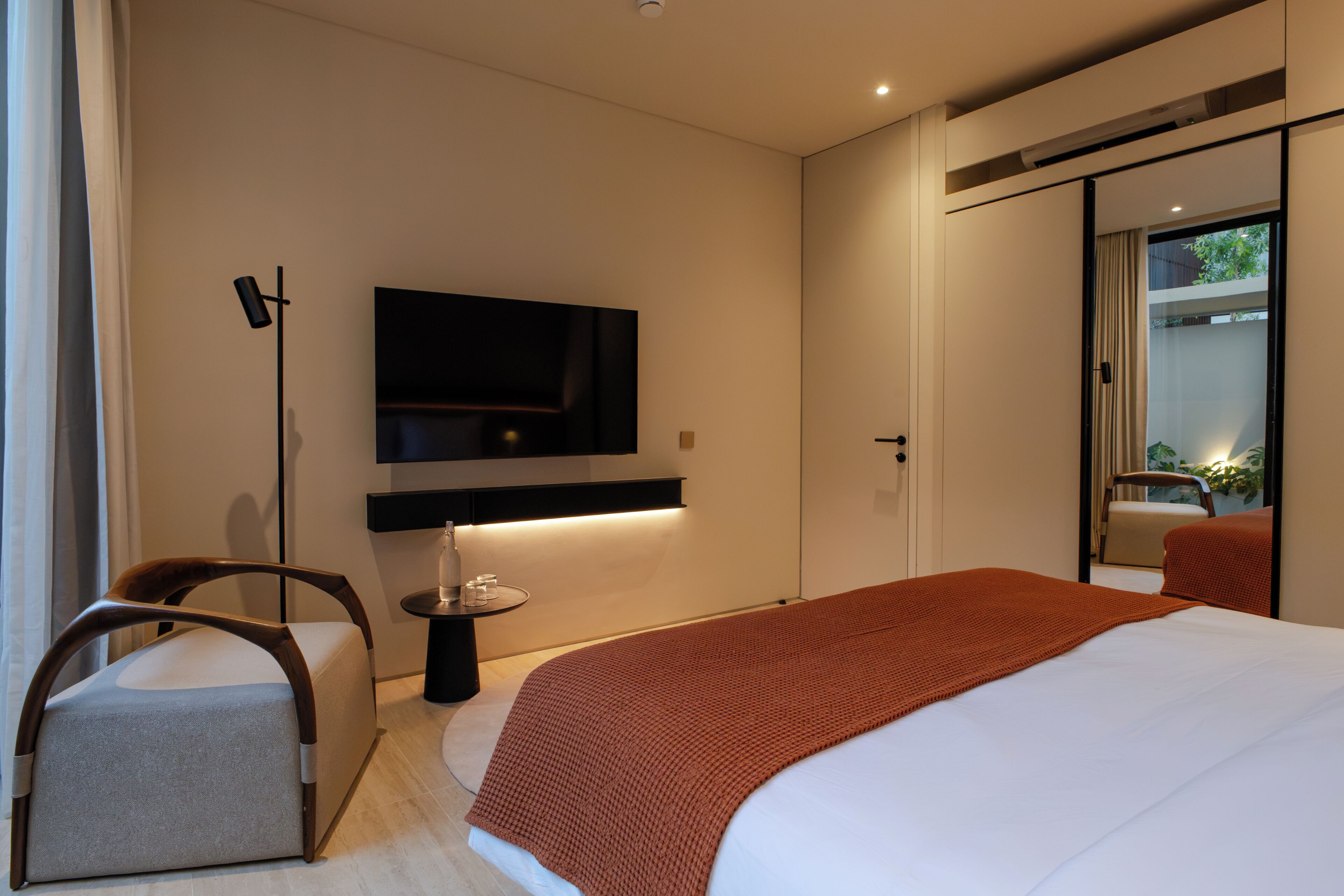 Moderni hotellihuone, jossa on suuri sänky, seinälle asennettu taulutelevisio, yöpöytä lampun kanssa ja tuoli.