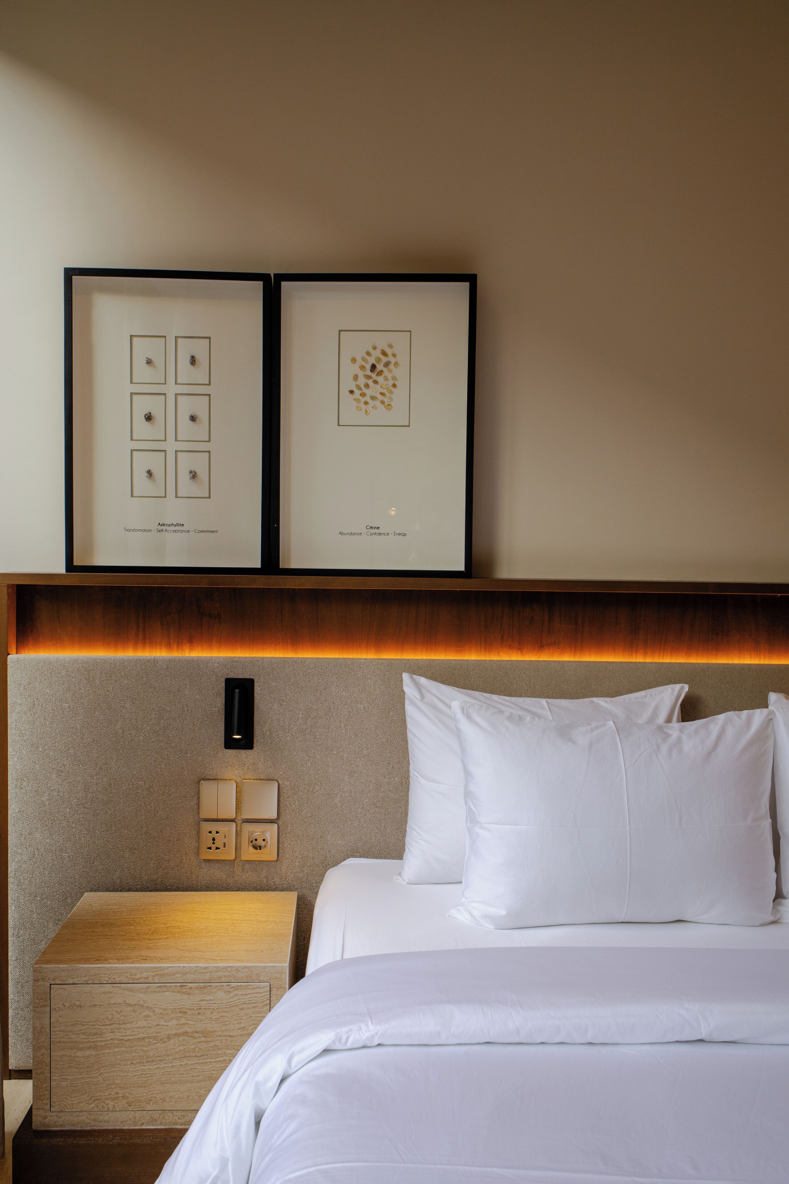 Une chambre d’hôtel avec un lit soigneusement fait, une table de chevet avec une lampe et deux œuvres d’art encadrées accrochées au mur.