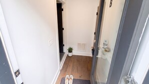 Un couloir avec une porte, une plante en pot, un paillasson et un porte-chaussures.