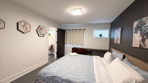 Une chambre moderne avec un grand lit, un bureau et une chaise. Deux œuvres d’art encadrées ornent le mur.