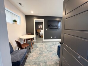 A modern living room with a flat-screen TV mounted on the wall, a round dining table with chairs, and a grey door. - Private 1BR King Suite • Near Downtown Nashville (Nashville)