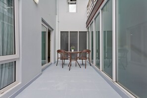 A corridor with a glass door, a potted plant, and wicker furniture. - The Studio - GrosvenorHouse (Muang Pattaya)