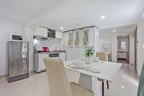 A modern kitchen with a refrigerator, microwave, and stove. There is a dining table with chairs and a vase with flowers. - The Studio - GrosvenorHouse (Muang Pattaya)