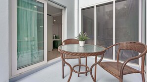 Taula amb tapa de vidre, cadires de vimetina i una planta en test, davant d'una paret blanca amb una porta corredissa de vidre que dona a una habitació.