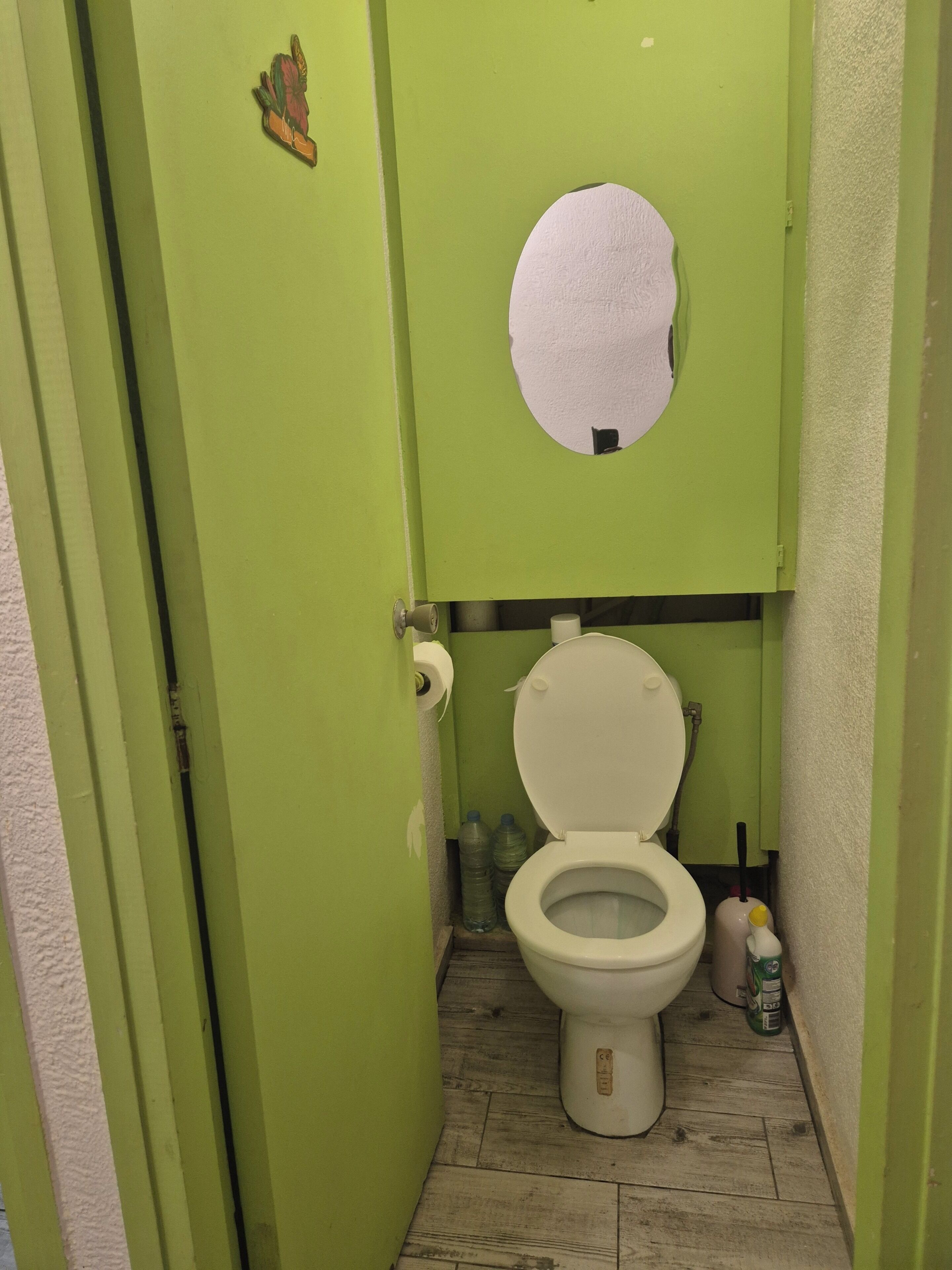 Un baño pequeño con inodoro, un rollo de papel higiénico y una botella de agua en el suelo.