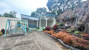 A playground with a slide and swings, surrounded by a landscaped garden with various shrubs and a rock wall. - Rehat at Linggarjati - Kuningan (Cilimus)