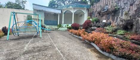 A playground with a slide and swings, surrounded by a landscaped garden with various shrubs and a rock wall.