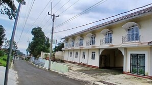 A two-story residential building with a balcony on the second floor, a gated entrance, and a street in front.