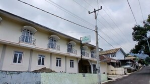 A multi-story residential building with balconies, a sign indicating a nearby location, and a street in the background.