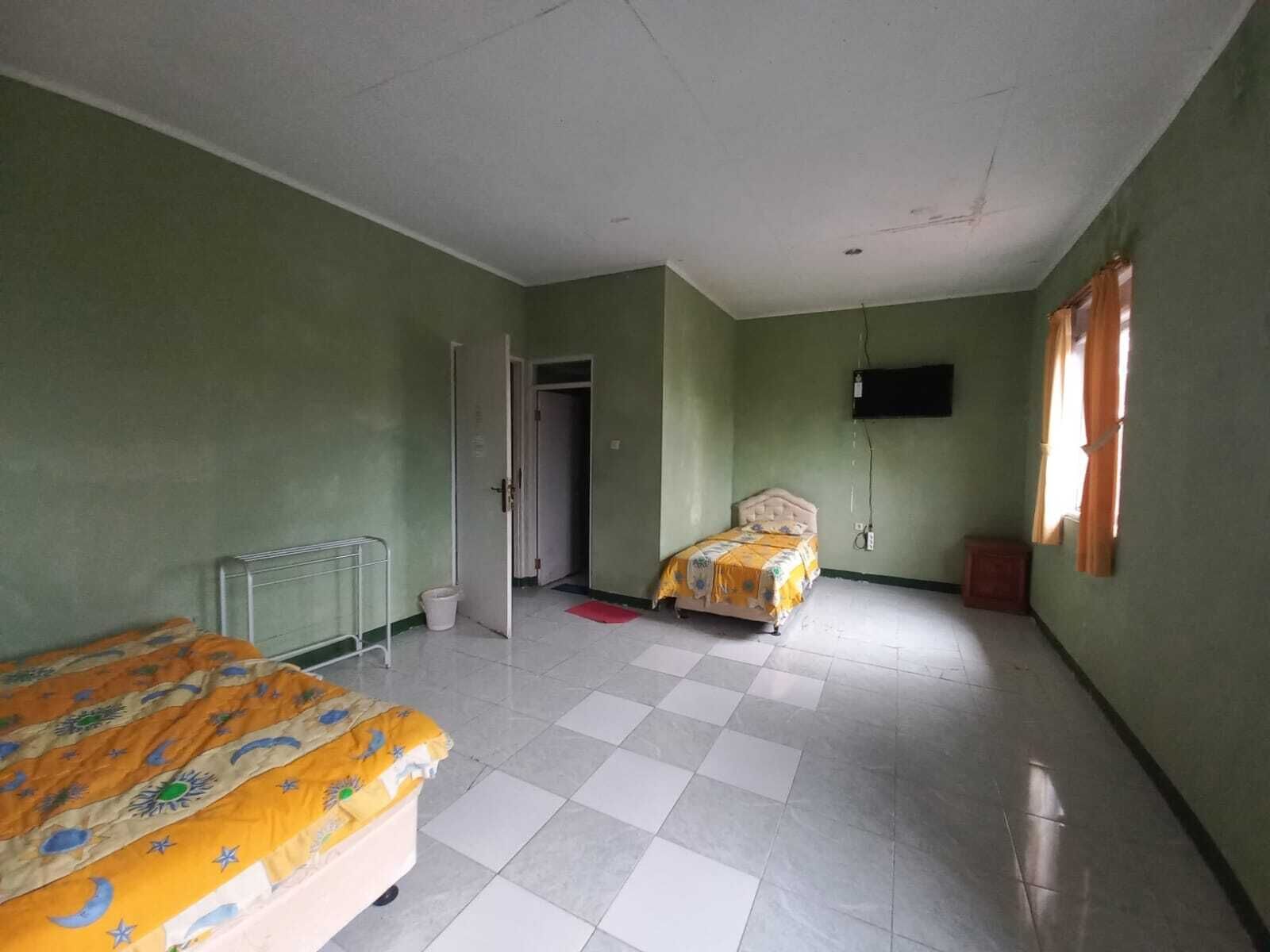 A room with two beds, a radiator, a television mounted on the wall, and a window with curtains.