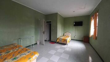 A room with two beds, a radiator, a television mounted on the wall, and a window with curtains.
