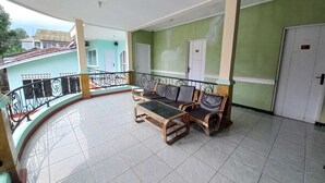 A balcony with a seating area, a tiled floor, and a view of a building in the background. - Rehat at Linggarjati - Kuningan (Cilimus)