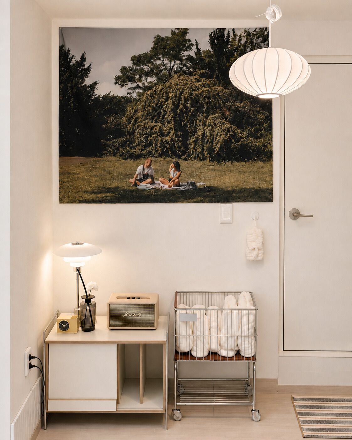 Una habitación con un cuadro grande enmarcado de una pareja en un campo, una lámpara, una radio antigua, una cuna para bebé y un radiador.