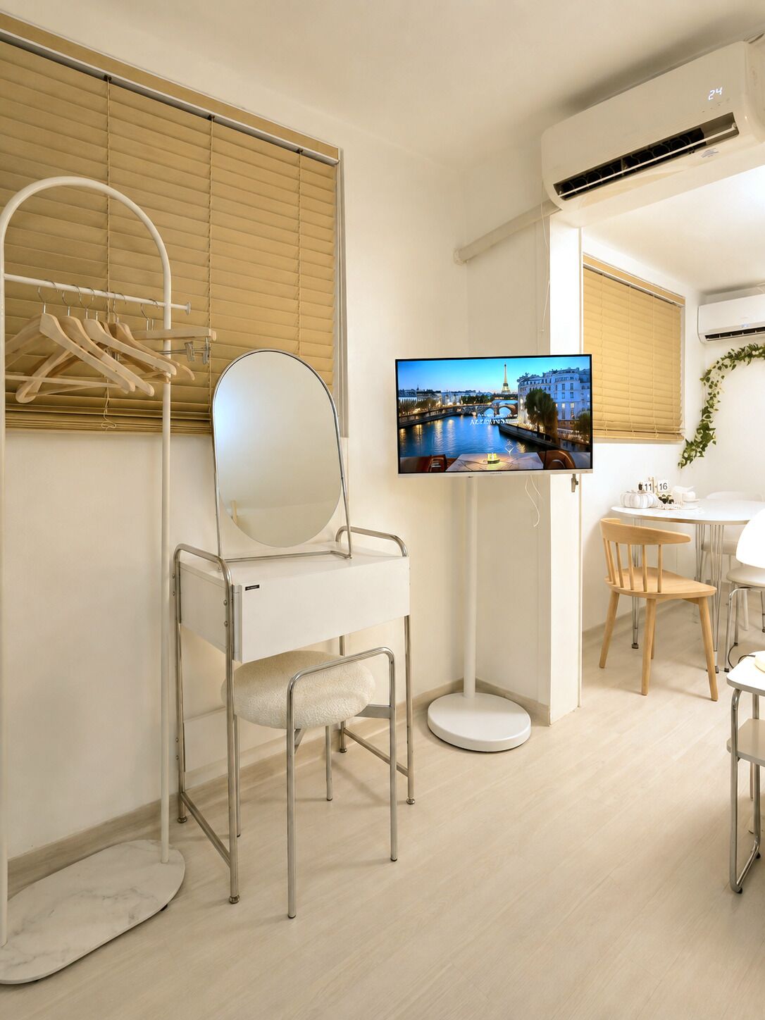 Habitación de hotel moderna con cama, televisor montado sobre un mueble, zona de comedor con mesa y sillas, y ventana con persianas.
