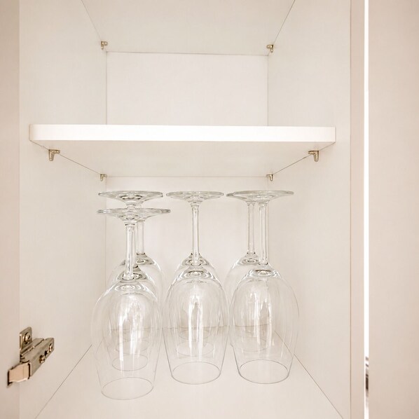 A white shelf with three wine glasses hanging from a metal rod.
