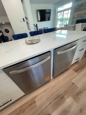 A modern kitchen with a white countertop, built-in dishwasher, and blue chairs.