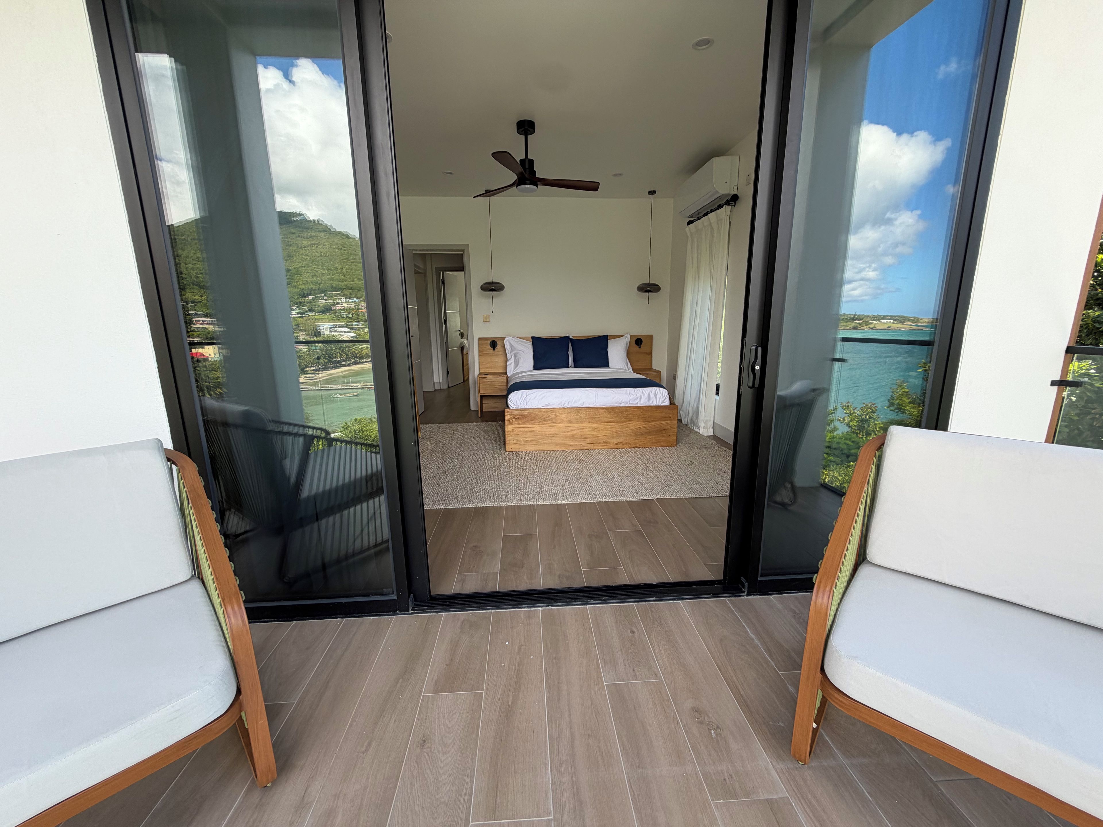 A bedroom with a bed, a ceiling fan, and a view of the sea through a sliding glass door.
