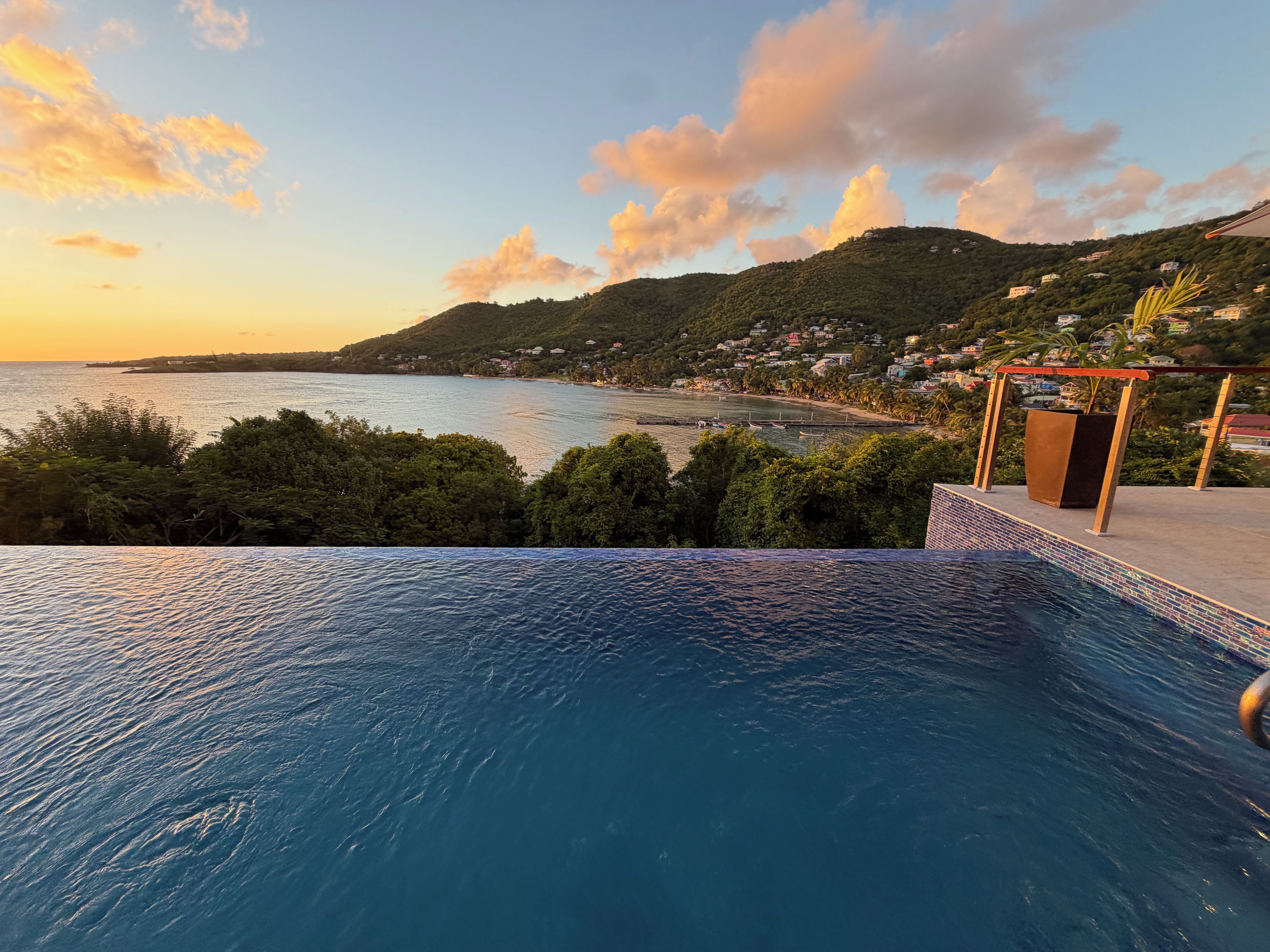 A swimming pool with a view of a coastal landscape and a hill with buildings.