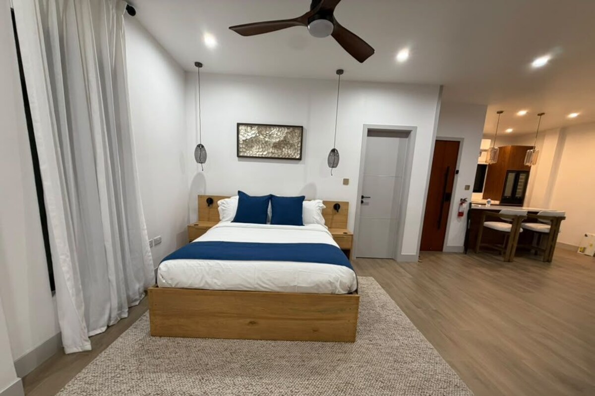 Un dormitorio moderno con una cama de madera, un ventilador de techo y un comedor con sillas.