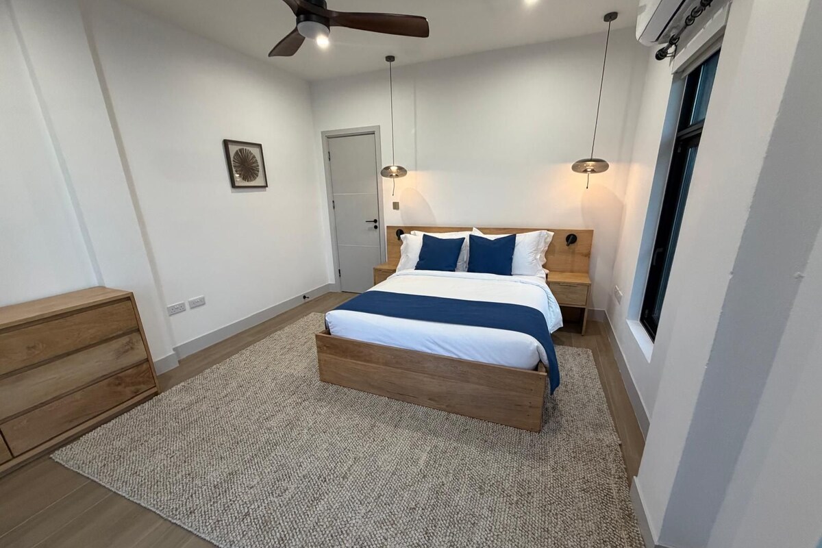 Un dormitorio con una cama de madera, un ventilador de techo, una mesita de noche y una ventana.