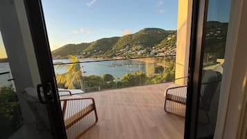 A balcony with a view of a coastal landscape, including hills and a body of water.