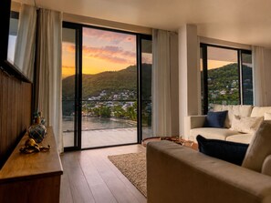 A modern living room with a sofa, a coffee table, and a view of a hillside town through large glass doors. - Palms La Batterie  (Laborie)