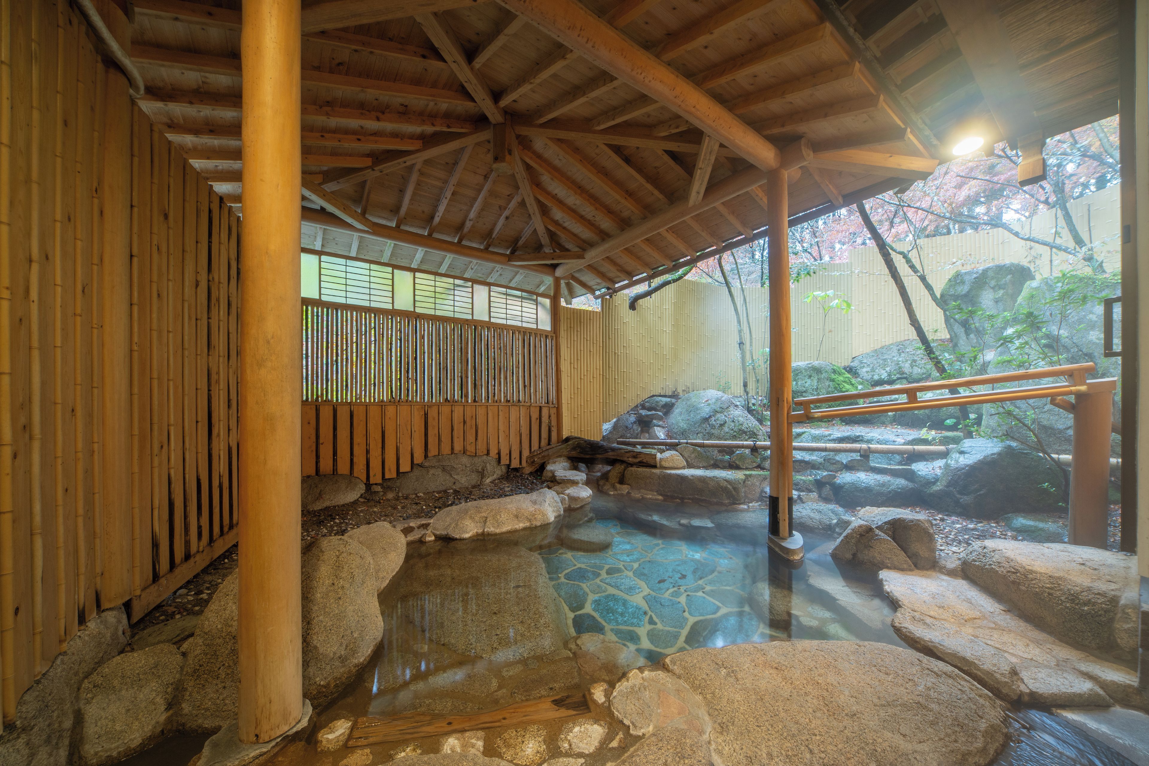 A traditional Japanese onsen with a wooden structure, stone hot spring bath, and a view of a natural landscape.