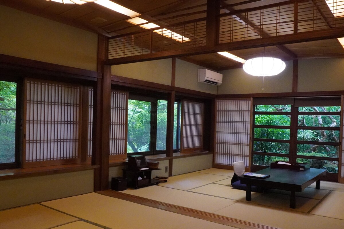 A traditional Japanese room with tatami flooring, sliding shoji doors, a tatami mat table, and a low ceiling with wooden beams.