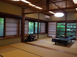 A traditional Japanese room with tatami flooring, sliding shoji doors, a tatami mat table, and a low ceiling with wooden beams.