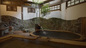 En traditionel japansk onsen med stenvæg, træbænk og en lille træbygning med et vandløb.