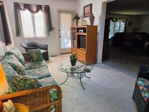 A living room with a sofa, a wicker chair, a glass coffee table, and a television on a wooden stand. - West Gate Retreat 3 bedroom home near Desoto Golf Club in Hot Springs Village (Hot Springs)