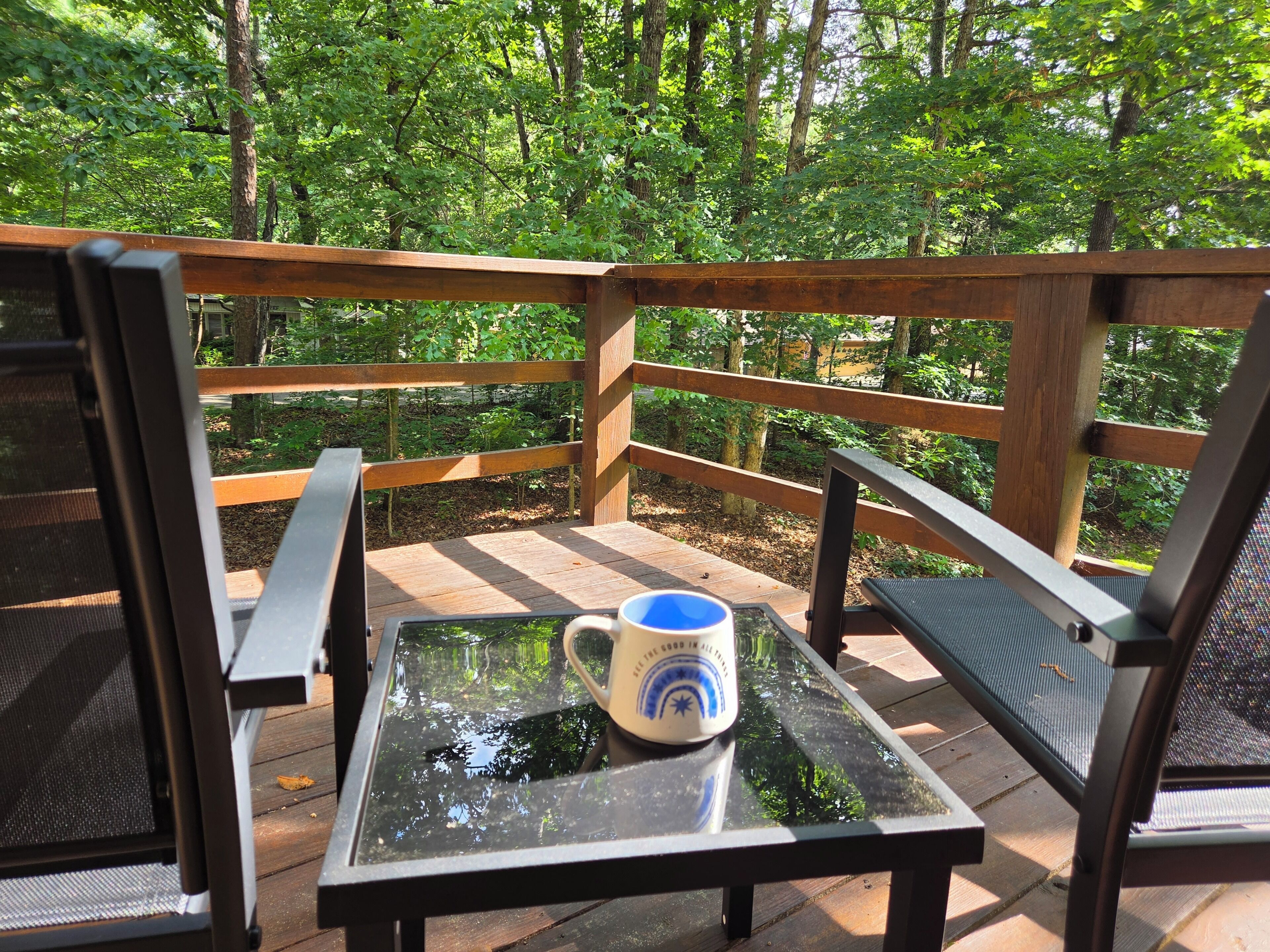 Eine Holzterrasse mit einem Glastisch und Stühlen, umgeben von einem Wald.