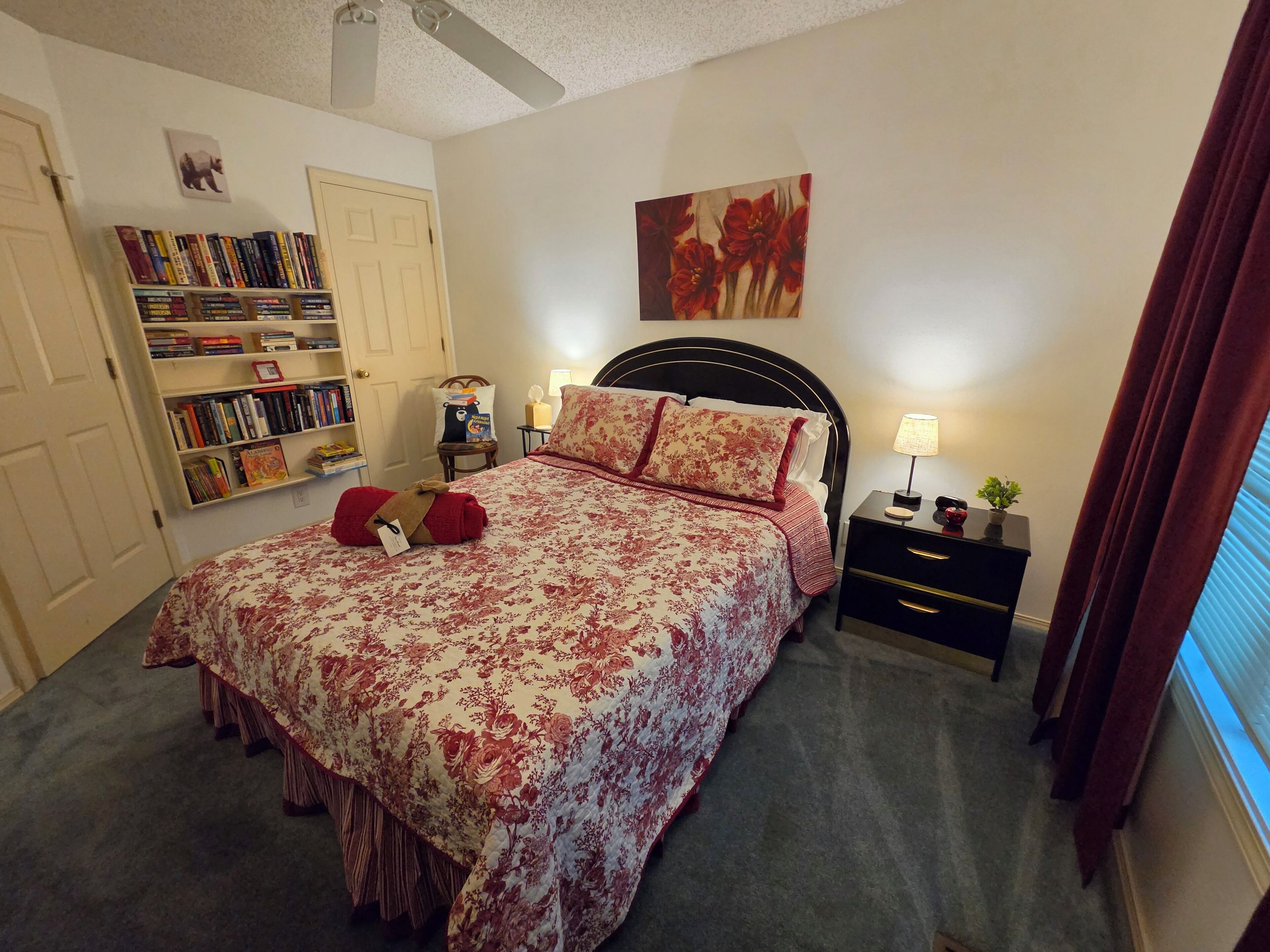 A bedroom with a bed, a bookshelf, a nightstand, and a window with curtains.